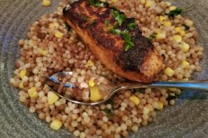 Grilled salmon on a bed of Israeli couscous in a bowl with a spoon.