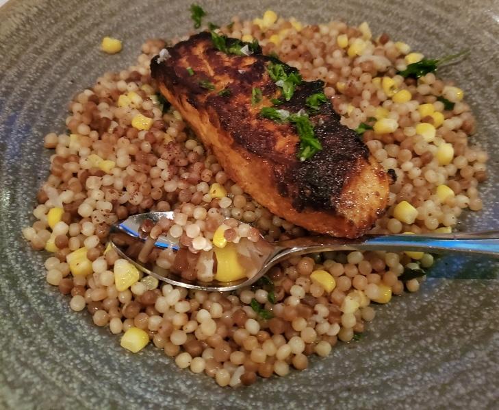 Grilled salmon on a bed of Israeli couscous in a bowl with a spoon.