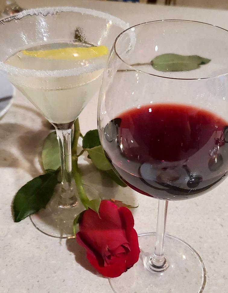 Lemon drop martini, glass of red wine and a rose on a white table cloth